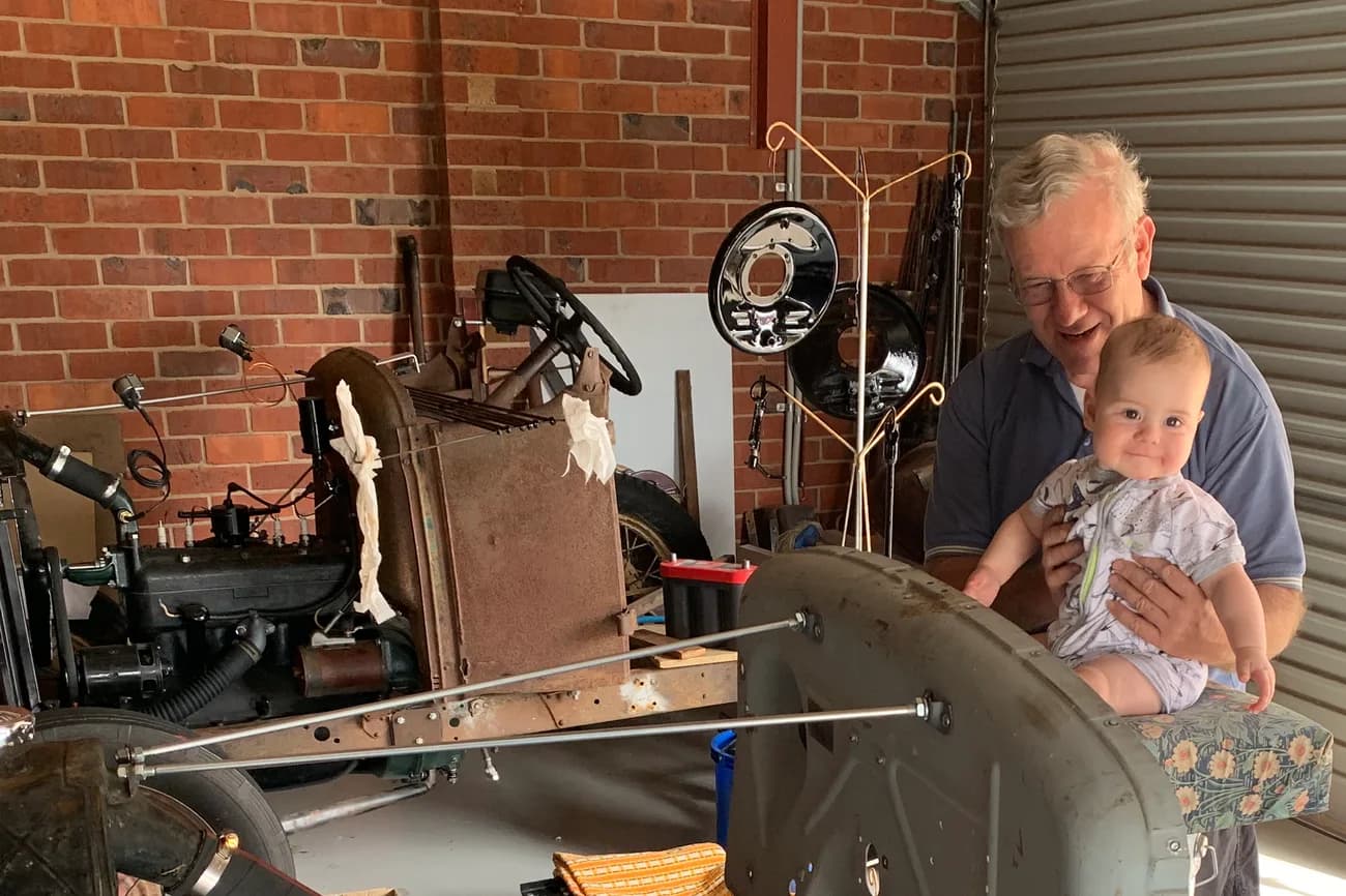 Dave with his grandson beside a Ford Model A chassis under restoration in the workshop